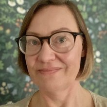 Headshot of Sini Rinne-Kerridge, NCVO Lead Consultant, wearing glasses and smiling in front of a floral wallpaper background.